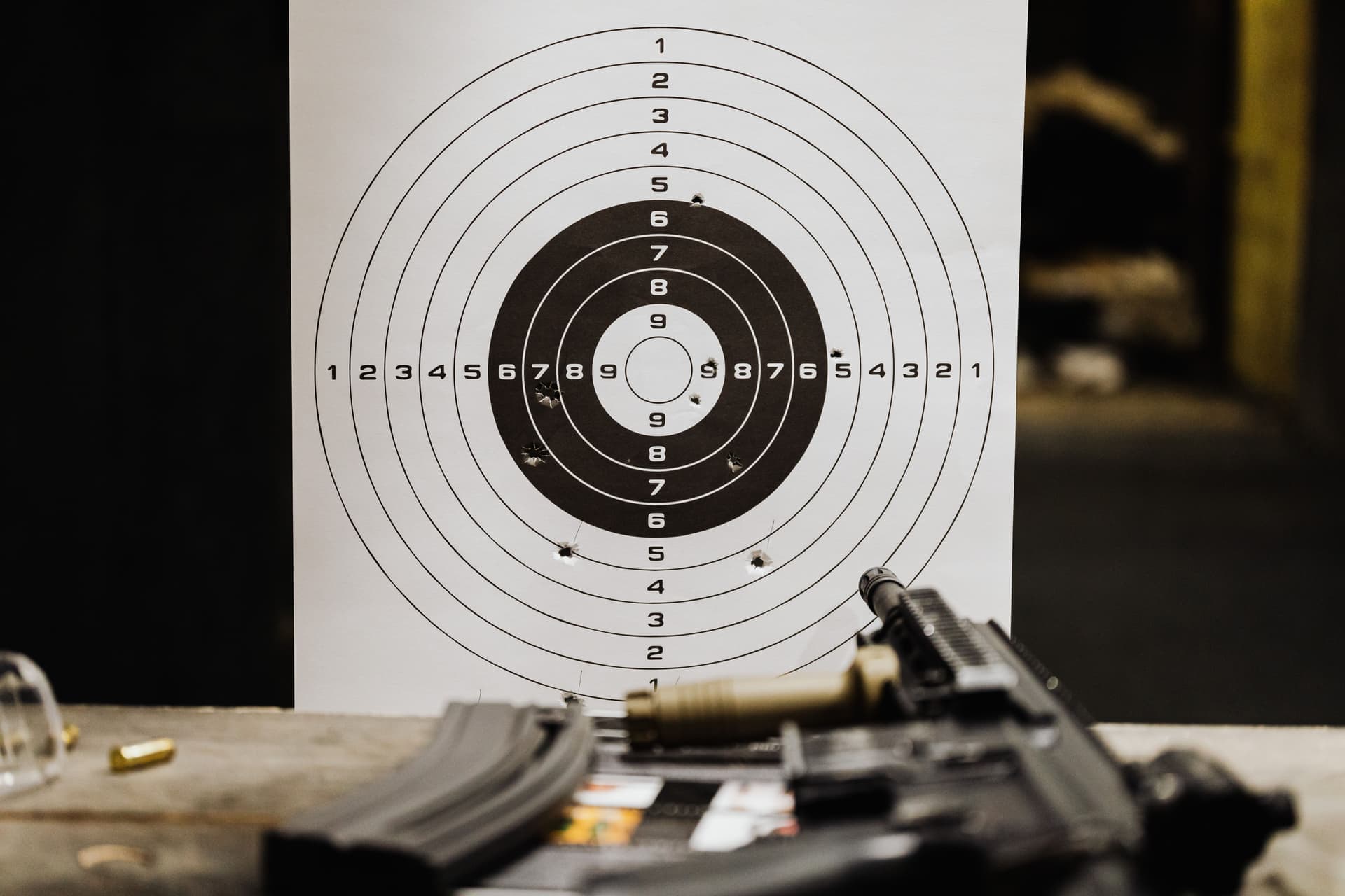 A paper target with bullet holes on a range table beside a rifle
