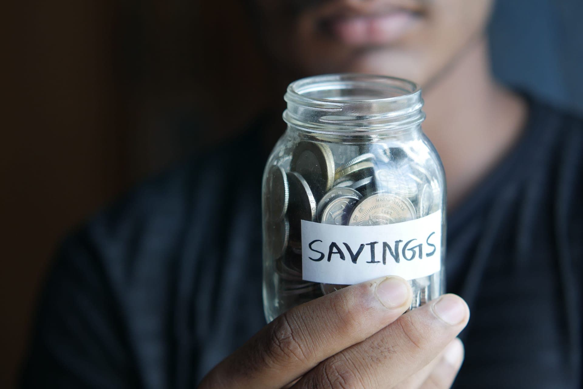 A hand holding a jar of coins labeled Savings