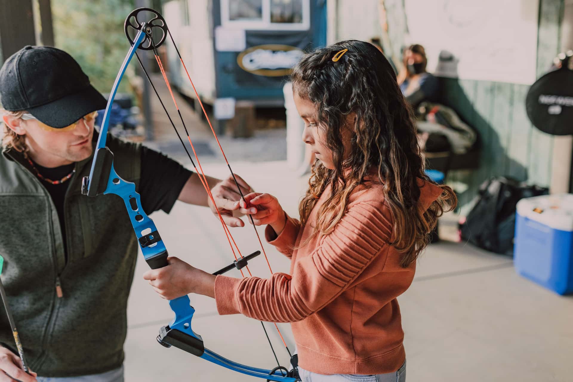 A girl practicing archery outdoors with an instructor