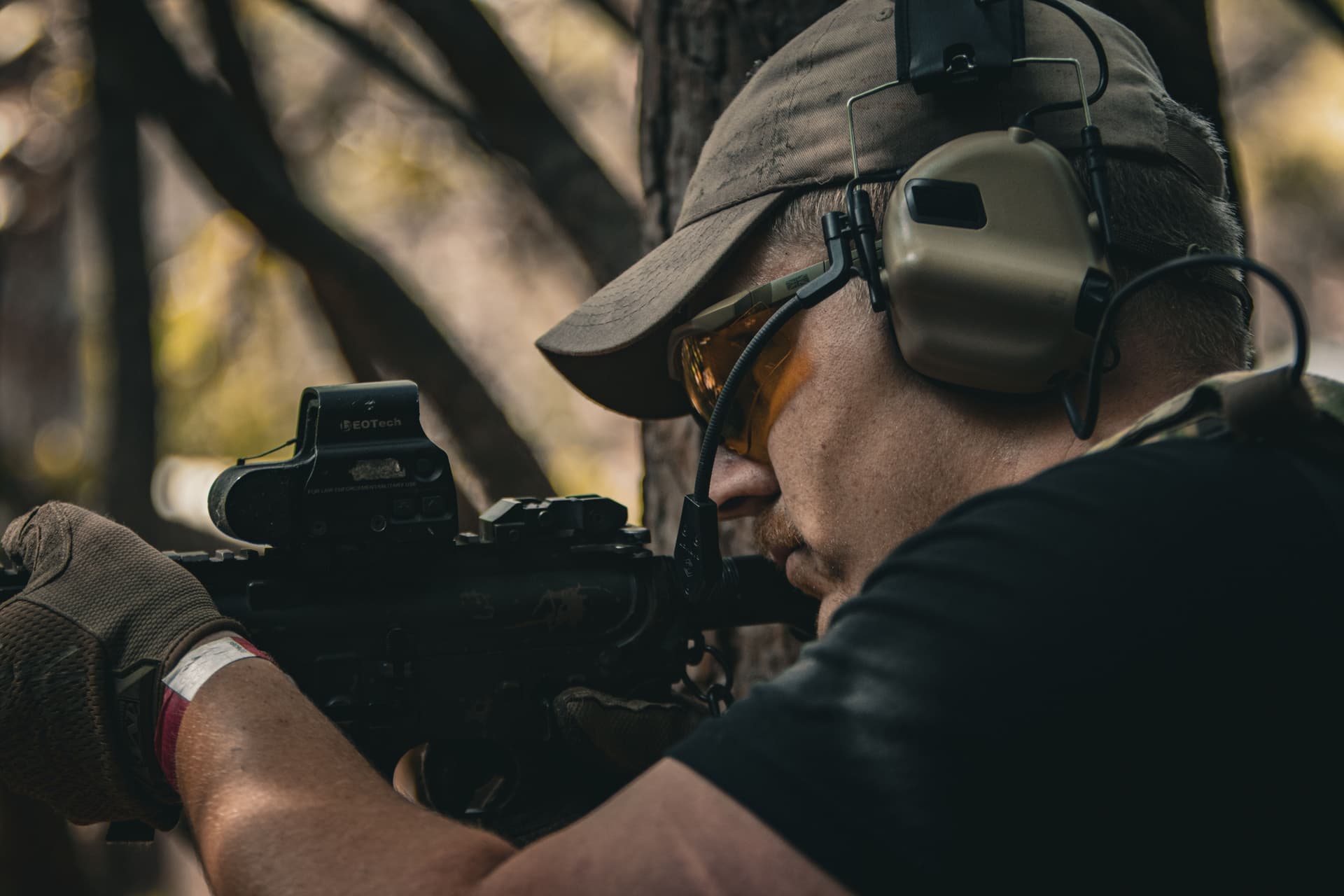 A soldier in tactical gear aiming a rifle outdoors