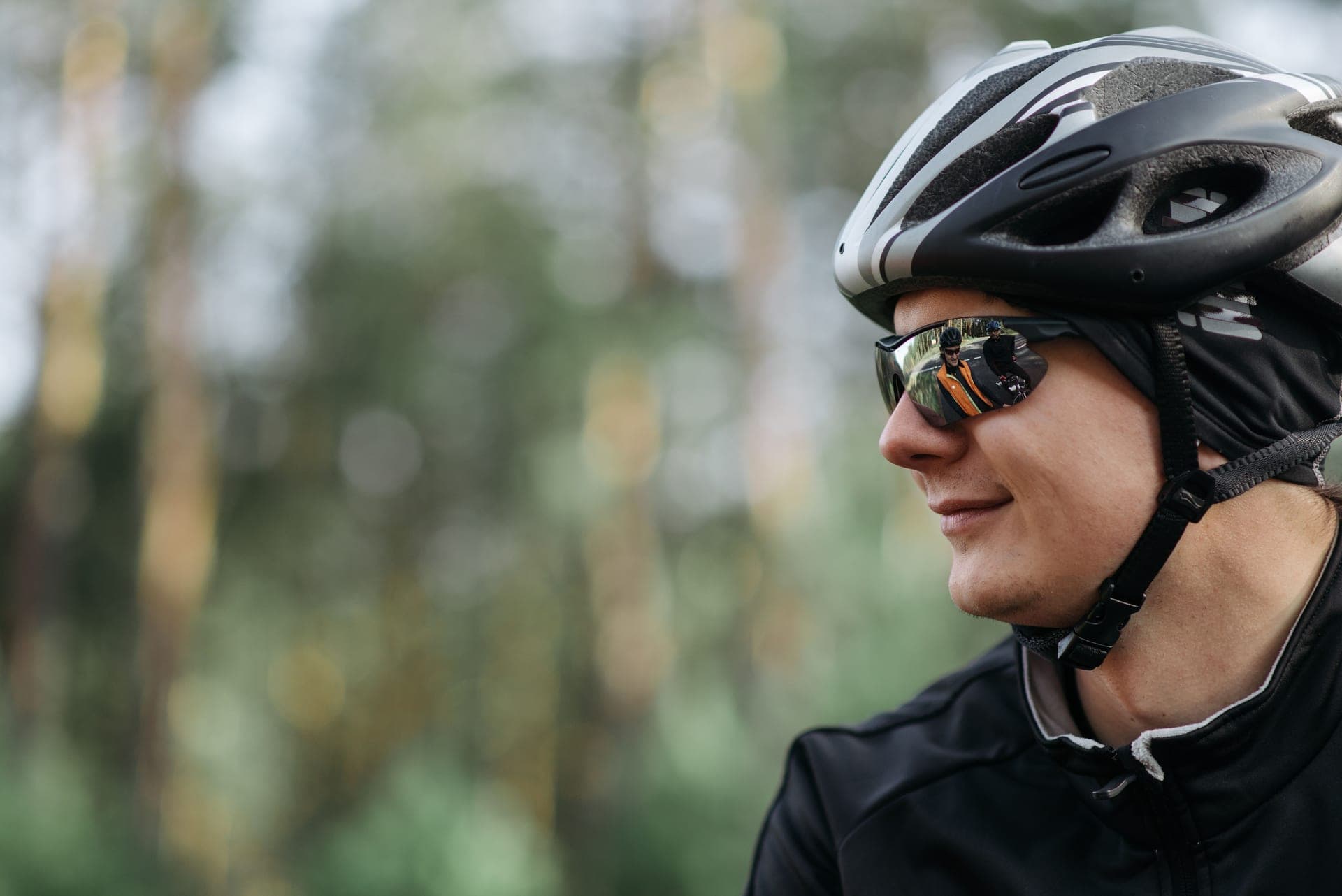 A cyclist in a helmet and sunglasses in a wooded area, in profile