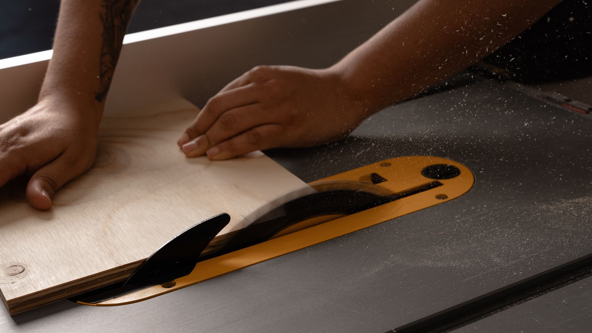 A person cutting wood on a table saw with sawdust in the air
