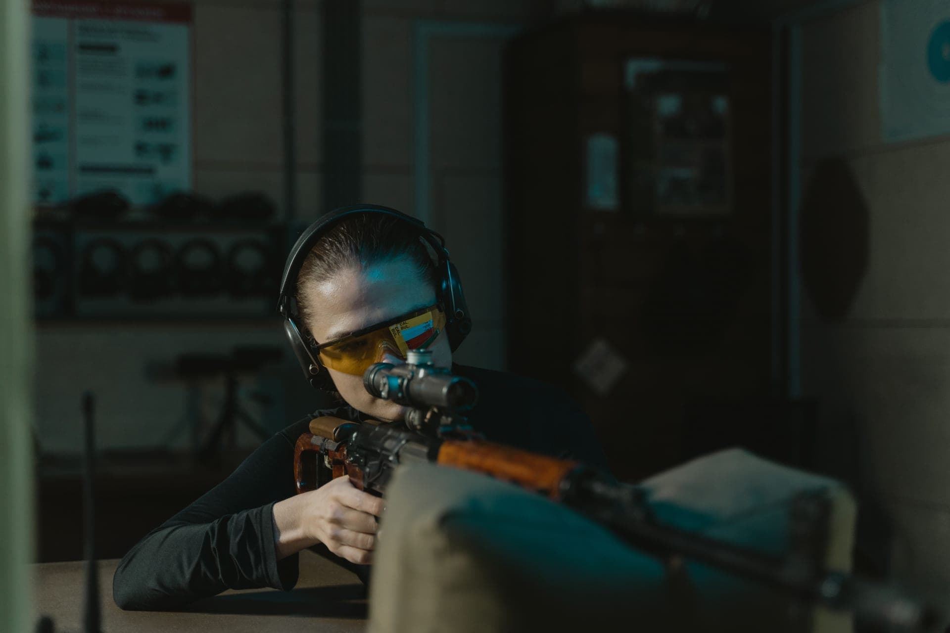 A woman aiming a rifle at a target on an indoor shooting range