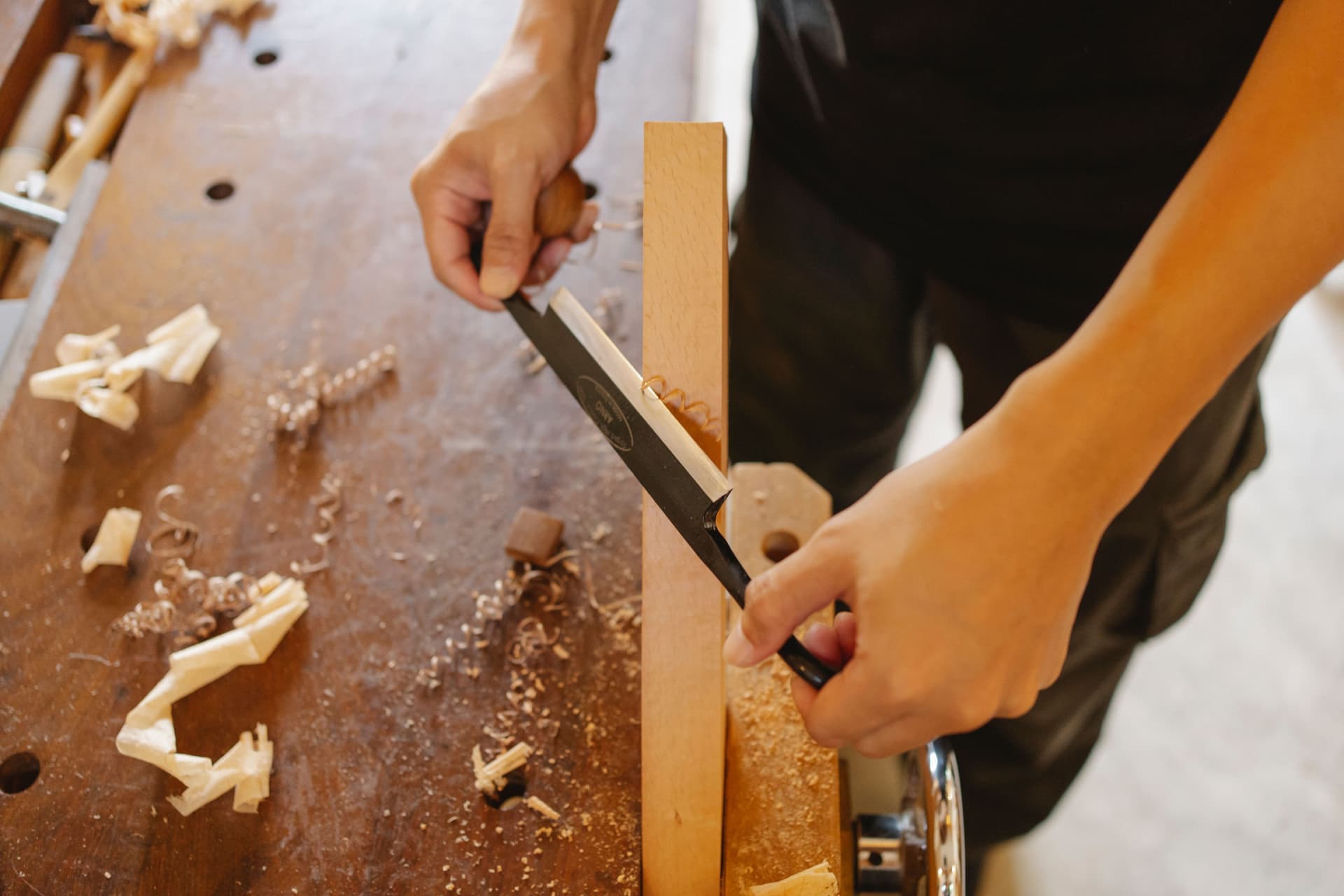 A craftsman cutting a wooden plank with a chisel, seen from above
